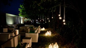 Un espacio al aire libre con mesas y sillas, rodeado de faroles decorativos y edificios pequeños.