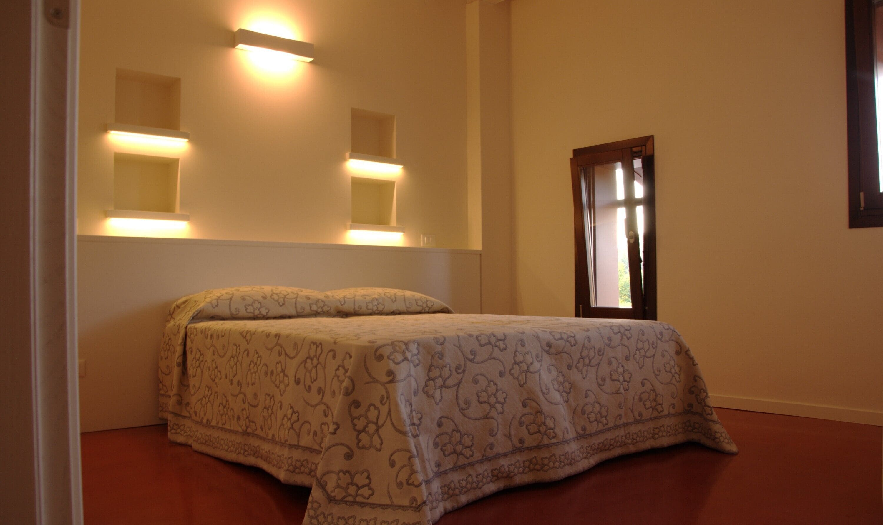 Un dormitorio con una cama, dos luces fijadas a la pared y un ventanal.