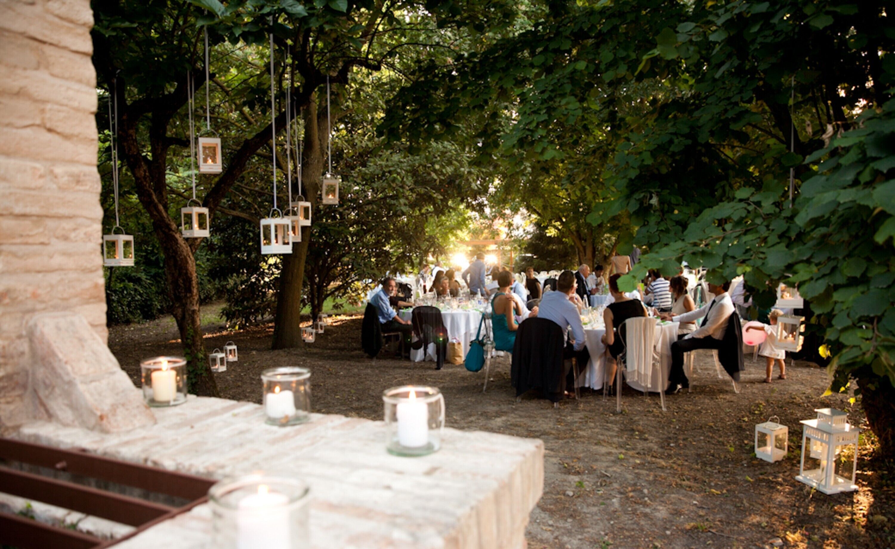 An outdoor event with tables set up under trees, surrounded by hanging lanterns.
