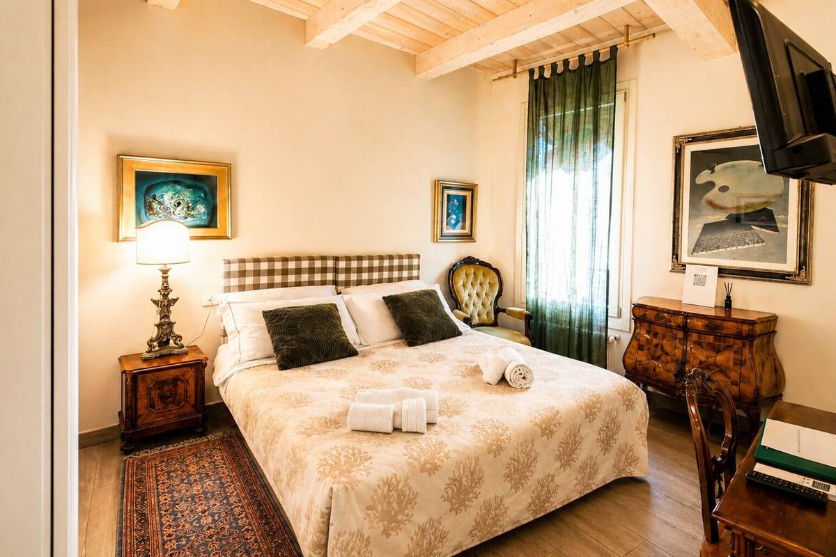 A bedroom with a bed, a nightstand, a lamp, a chair, a desk, and a painting on the wall.