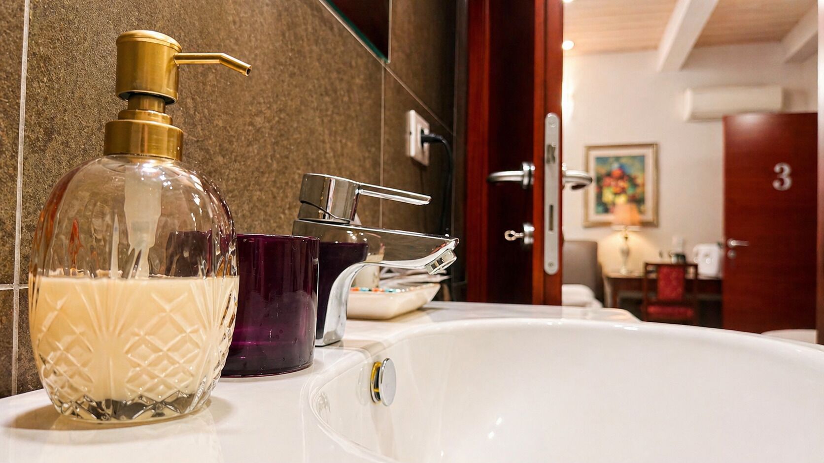 Une salle de bain avec un lavabo blanc, un distributeur de savon doré et un porte-savon violet.