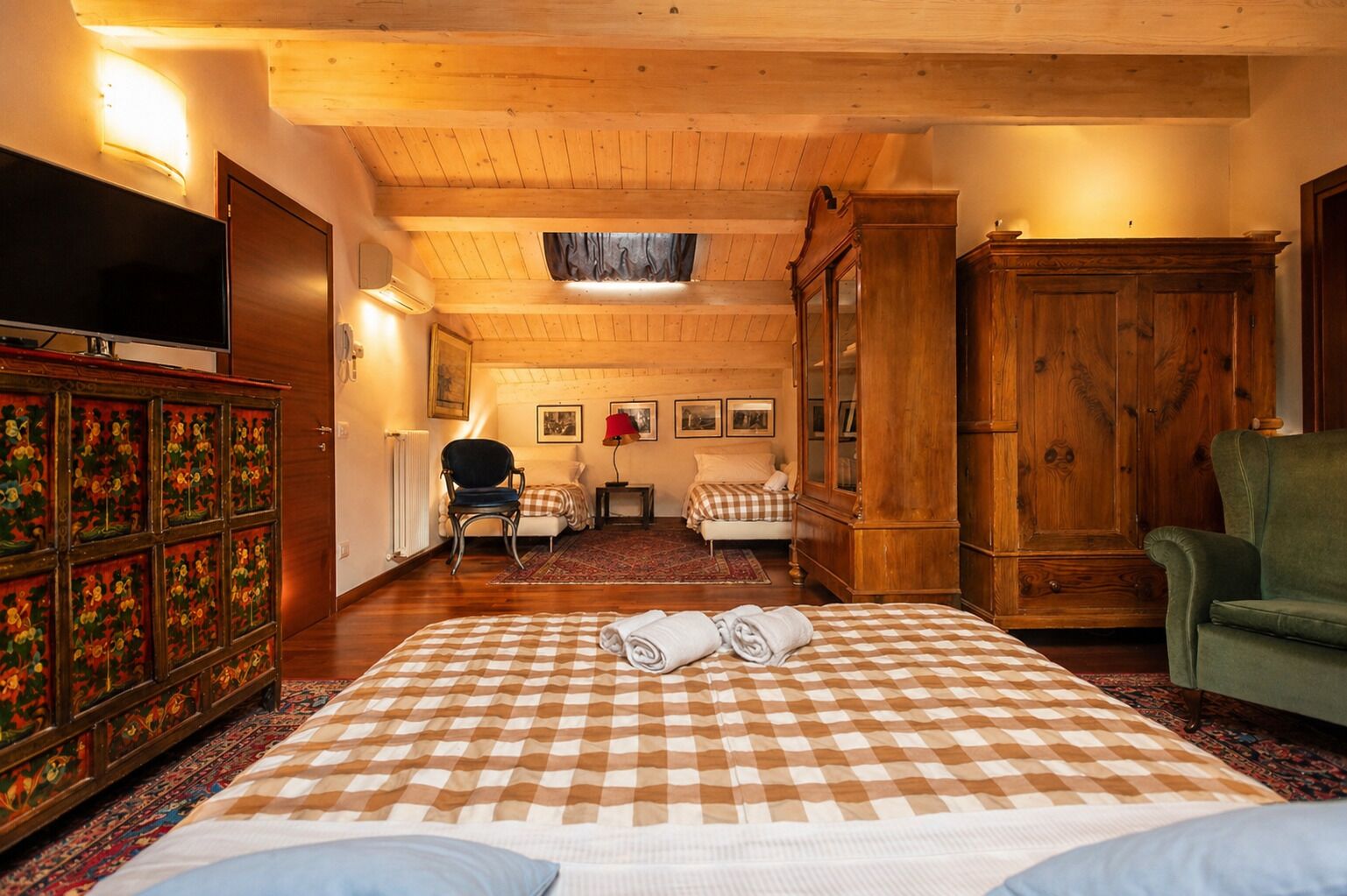 A room with a checkered bedspread, a wooden cabinet, a television, and a green armchair.