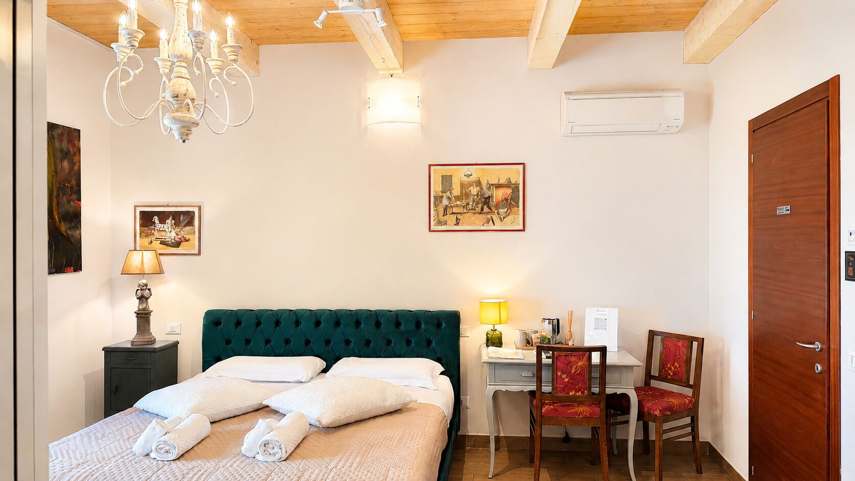 Ein Schlafzimmer mit einem Bett, einem Schreibtisch, einem Stuhl, einer Chandelier und Kunstwerken an den Wänden.