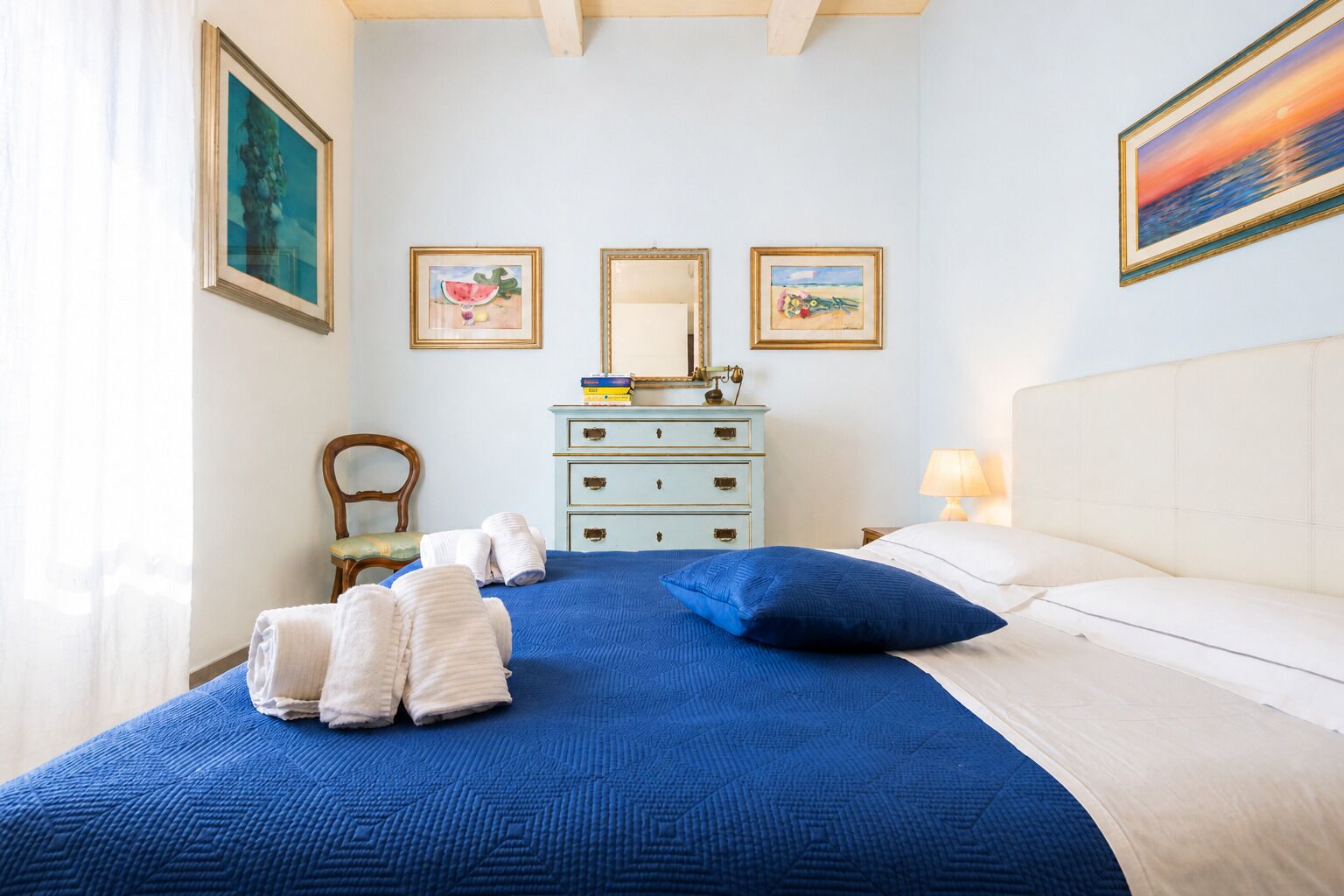 A bedroom with a bed, a dresser, a chair, and artwork on the walls.