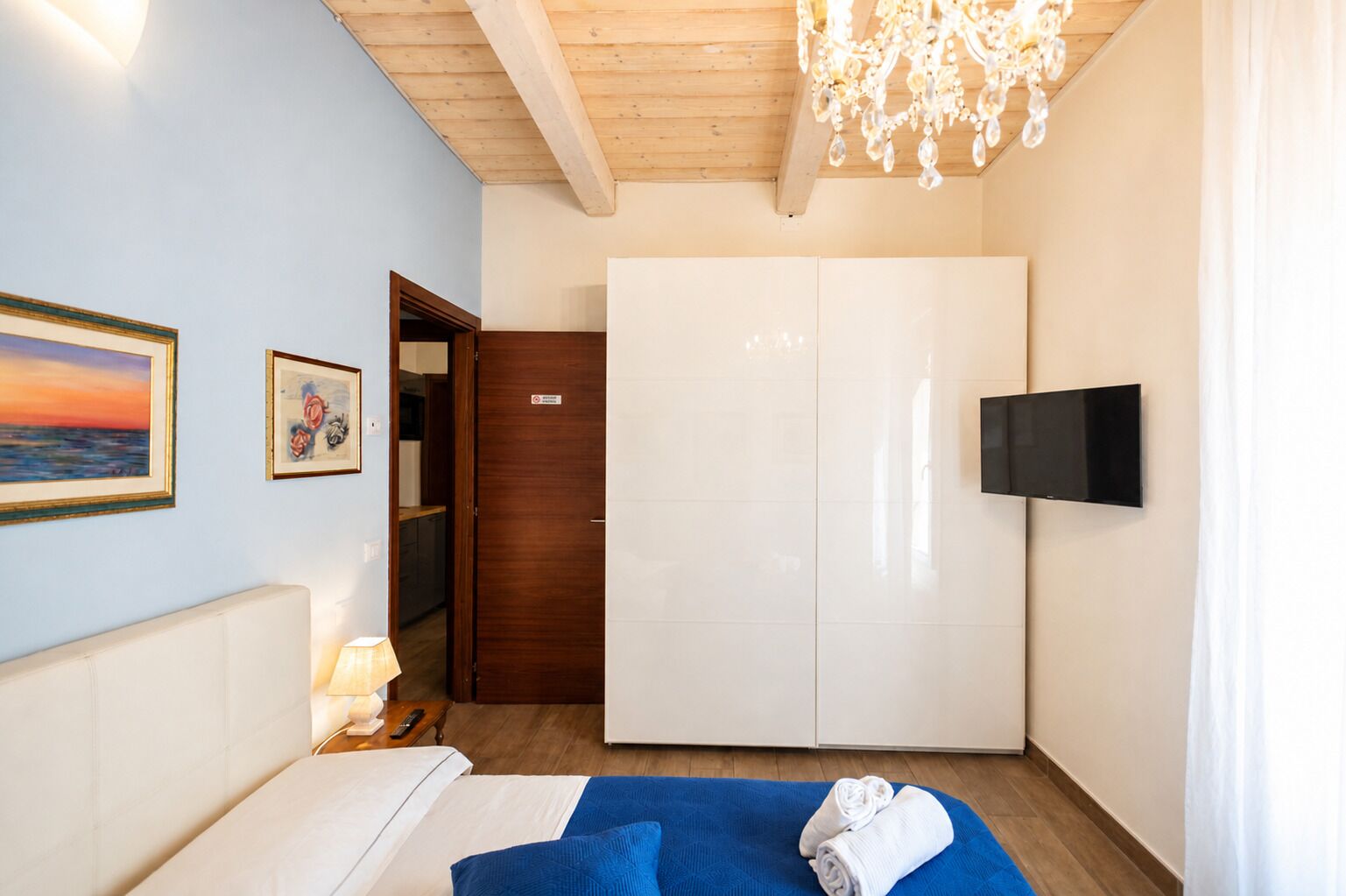 Habitación de hotel con cama, televisor, armario, un cuadro y una araña.