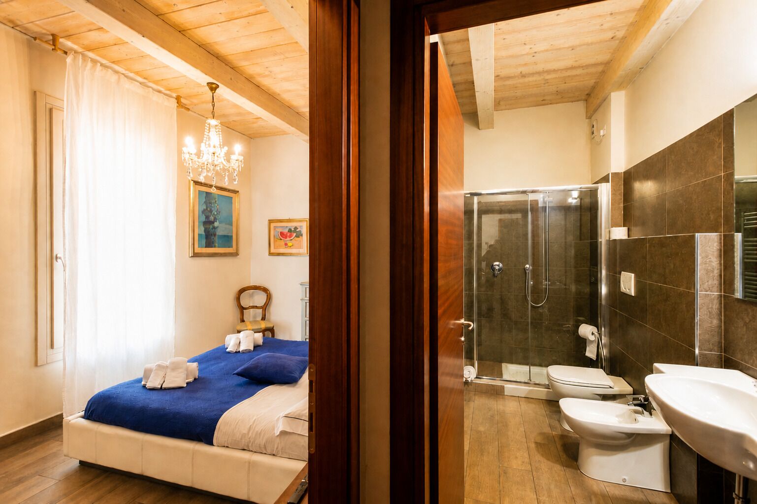 Ein Schlafzimmer mit Bett, einer Chandelierleuchtre und einem Duschbad mit Toilette und Waschbecken.
