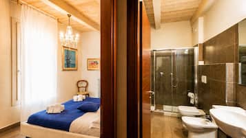 Ein Schlafzimmer mit Bett, einer Chandelierleuchtre und einem Duschbad mit Toilette und Waschbecken.