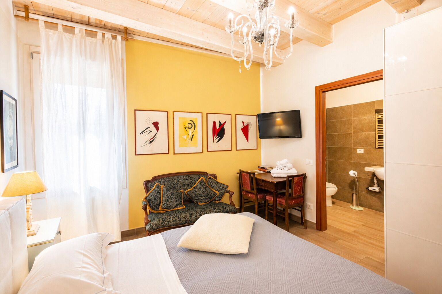 A hotel room with a bed, a desk, a chair, a TV, and artwork on the wall.