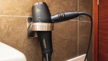 Un sèche-cheveux fixé au mur, qui est recouvert de carreaux, dans une salle de bain.