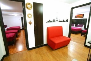 Habitación de hotel con sofá rojo, cama con colcha roja y morada, y un cuadro mural con vista urbana.