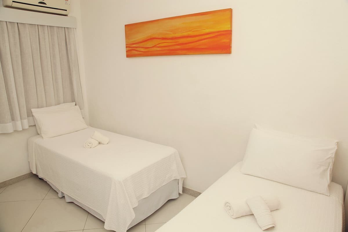 A hotel room with two beds, a painting on the wall, and a window with curtains.
