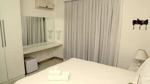 Habitación de hotel con cama, tocador con espejo, teléfono y aire acondicionado instalado en la pared.