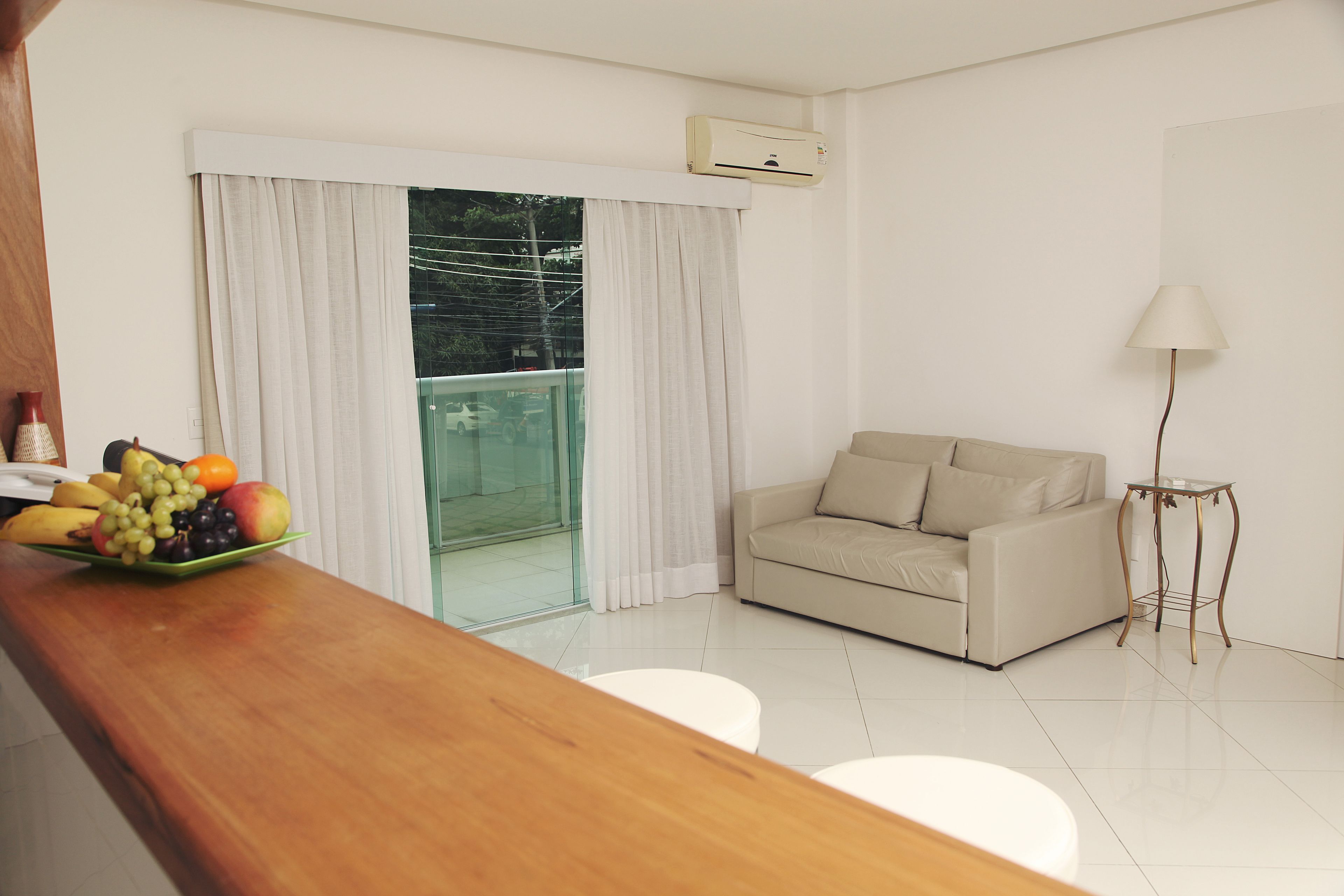 Ein modernes Wohnzimmer mit einer Couch, einem Esstisch mit Obst, einer Lampe und einer Glastür zum Balkon.