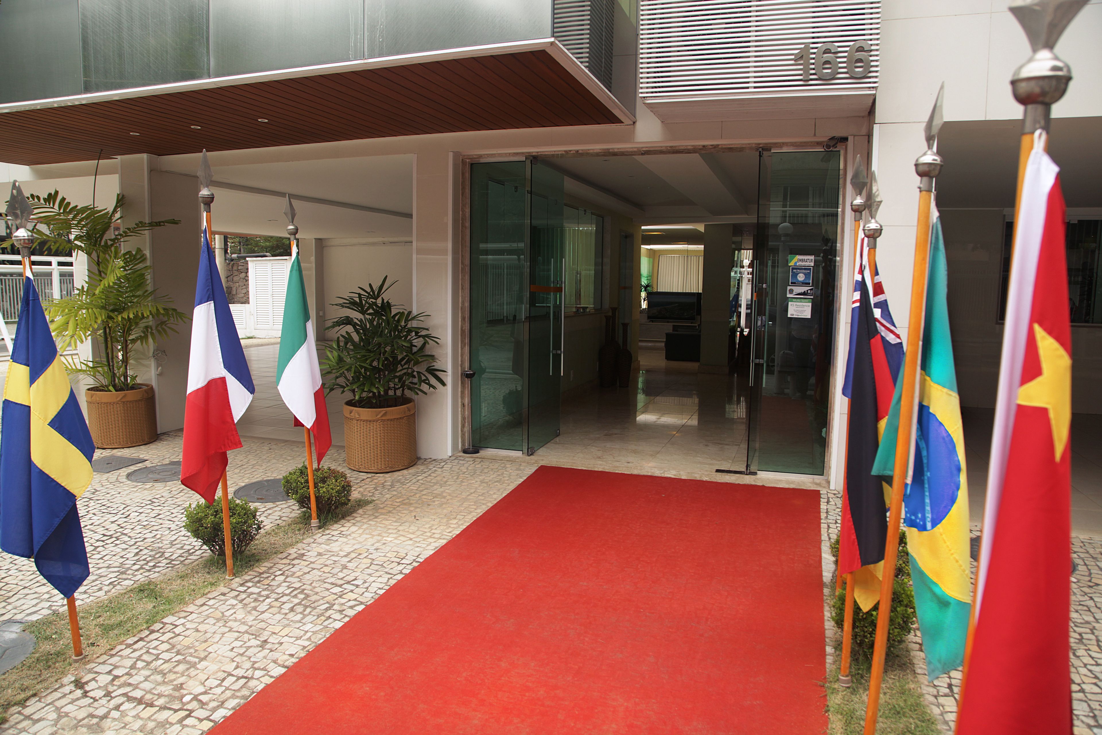 A hotel entrance with a red carpet, multiple flags, and potted plants.