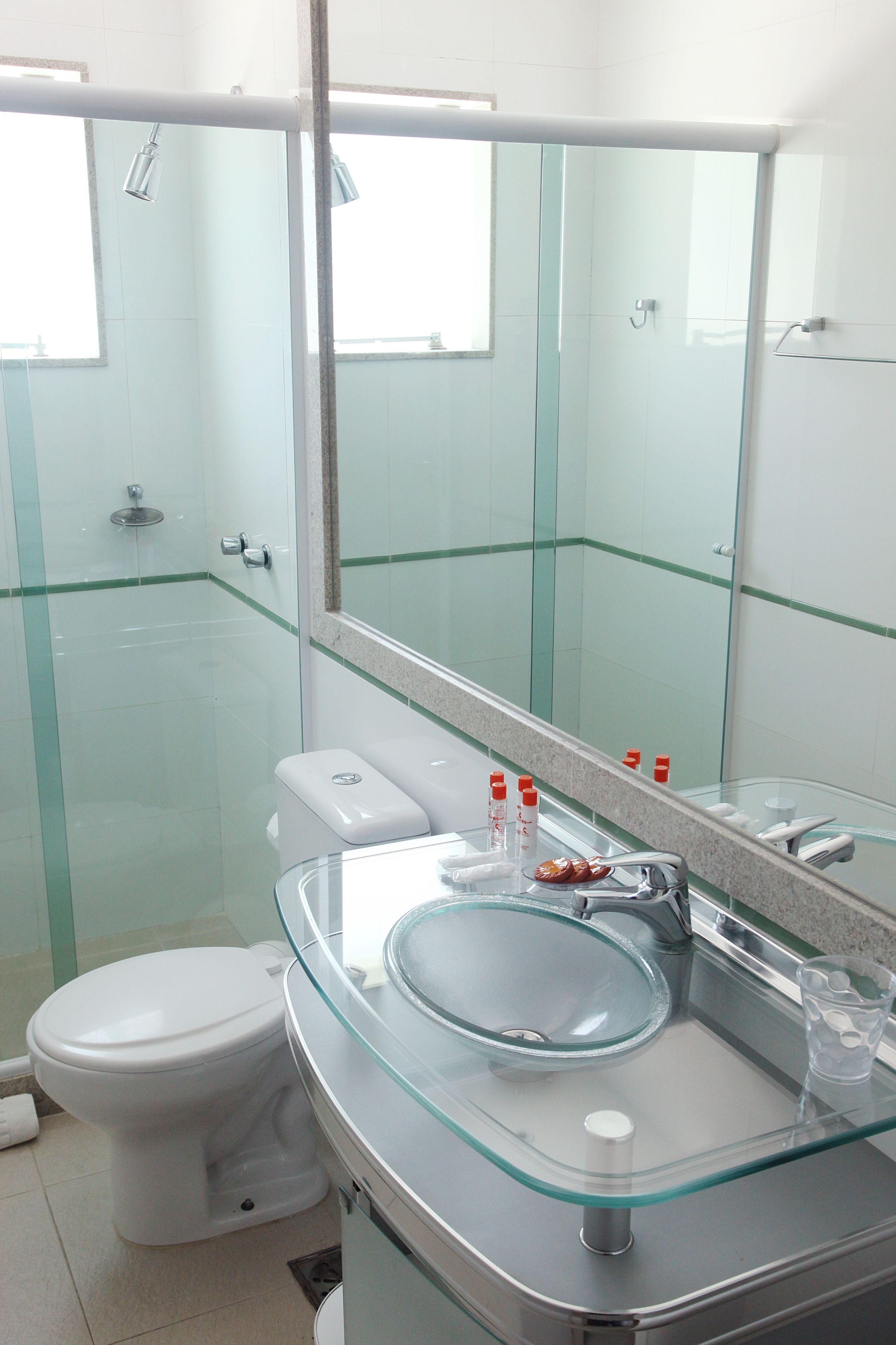 A modern bathroom with a glass shower enclosure, a white toilet, a glass sink, and a large mirror.