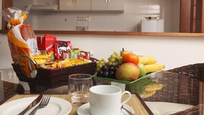 Una escena de desayuno con una cesta de frutas, una taza blanca y un vaso sobre una mesa.