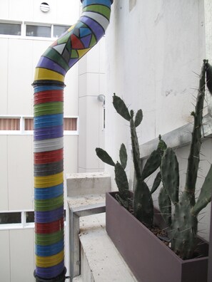 A colorful, multicolored pipe structure adjacent to a building with a white exterior and a cactus plant in a brown planter. - Infinito Hotel (Buenos Aires)
