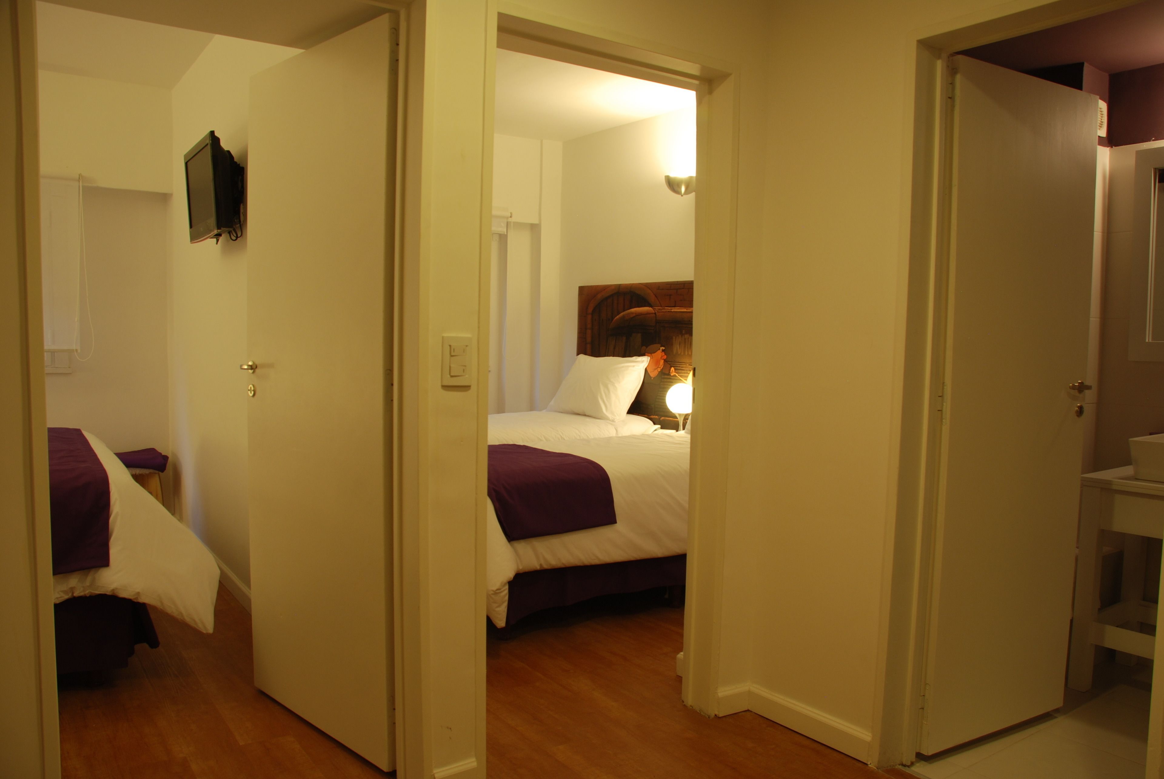 Una habitación de hotel con dos camas, un televisor en la pared y un cabecero de madera.