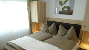 A double bed with a white and beige bedspread, a wooden headboard, and two bedside tables with lamps. - Eden (SAAS GRUND)