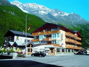 A hotel with a traditional Alpine architectural style, featuring a multi-story building with balconies and a mountain backdrop. - Eden (SAAS GRUND)