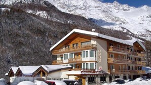 A multi-story hotel with a wooden facade, balconies, and a view of snow-covered mountains. - Eden (SAAS GRUND)