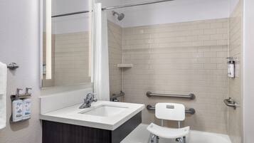 A modern bathroom with a white sink, mirror, and shower. It includes a grab bar and a white toilet.