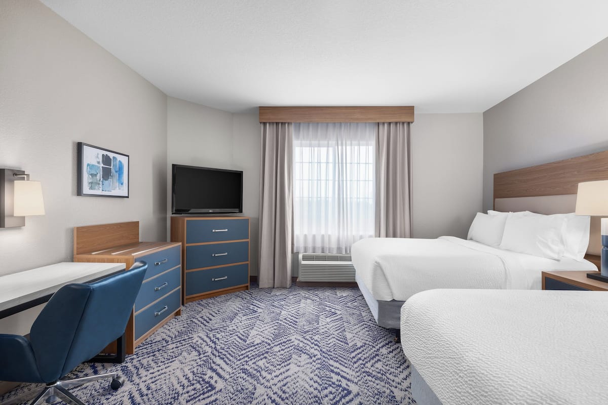 Habitación de hotel con cama, escritorio, silla, televisor y ventana con cortinas.