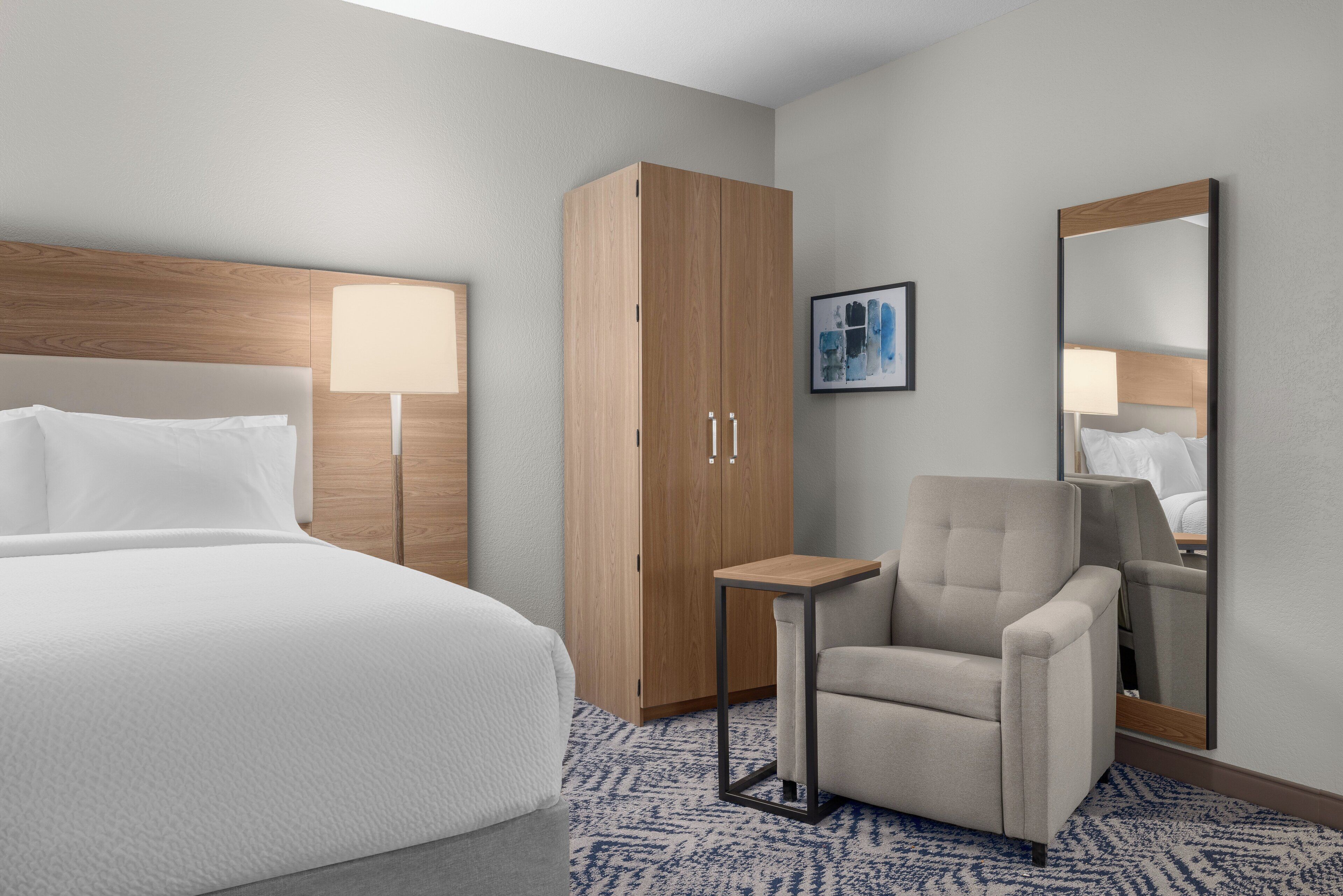 A hotel room with a large bed, a wooden wardrobe, a small table, a chair, and a mirror.