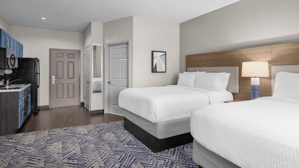 A hotel room with two beds, a desk with a computer, a TV, and a blue patterned rug. - Candlewood Suites Alexandria by IHG (Alexandria)