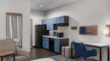 A hotel room with a kitchenette, a bed, a desk, and a chair.