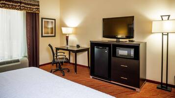 Habitación de hotel con cama, escritorio con silla, televisión, microondas y lámpara.