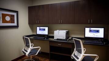 A room with two desks, each with a computer and a printer, and two office chairs.