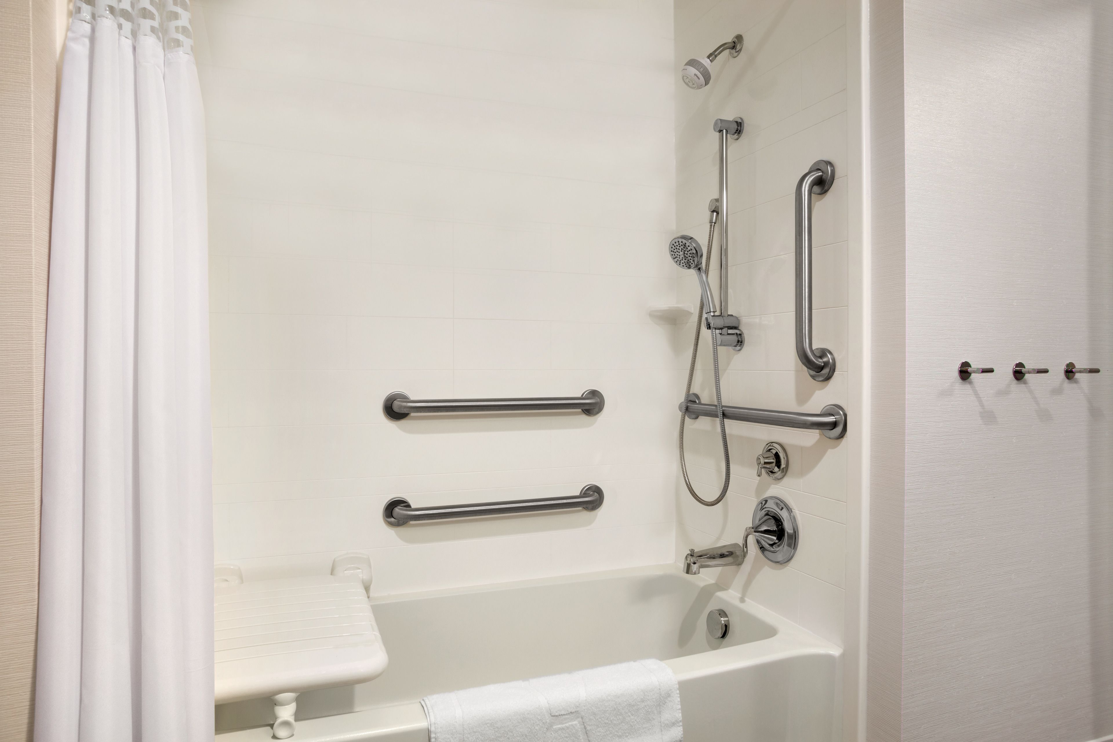 A bathroom with a white bathtub, grab bars, a showerhead, and a towel rack.