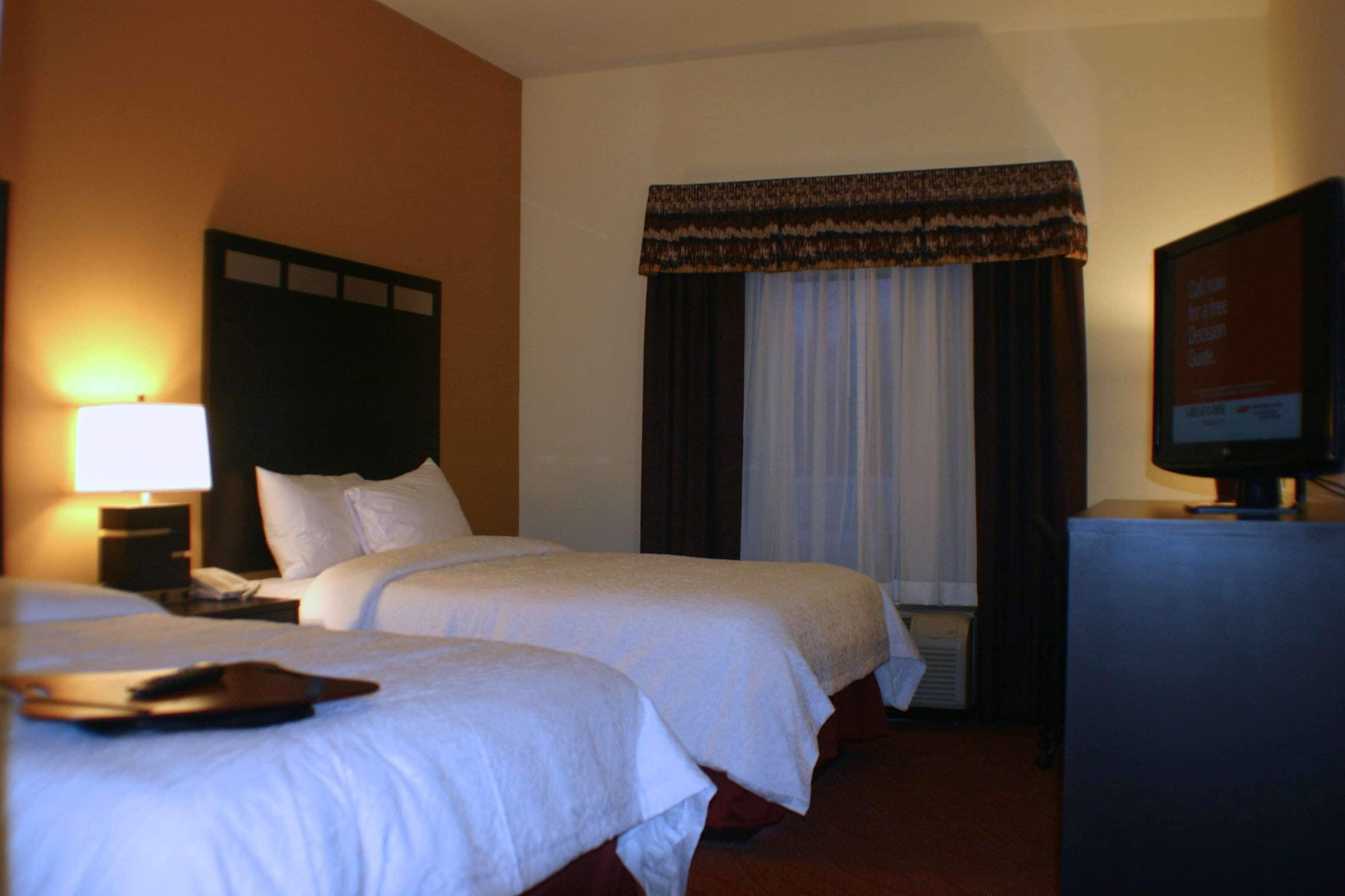 Ein Hotelzimmer mit zwei Betten, einem Fernseher und einem Fenster mit Vorhängen.