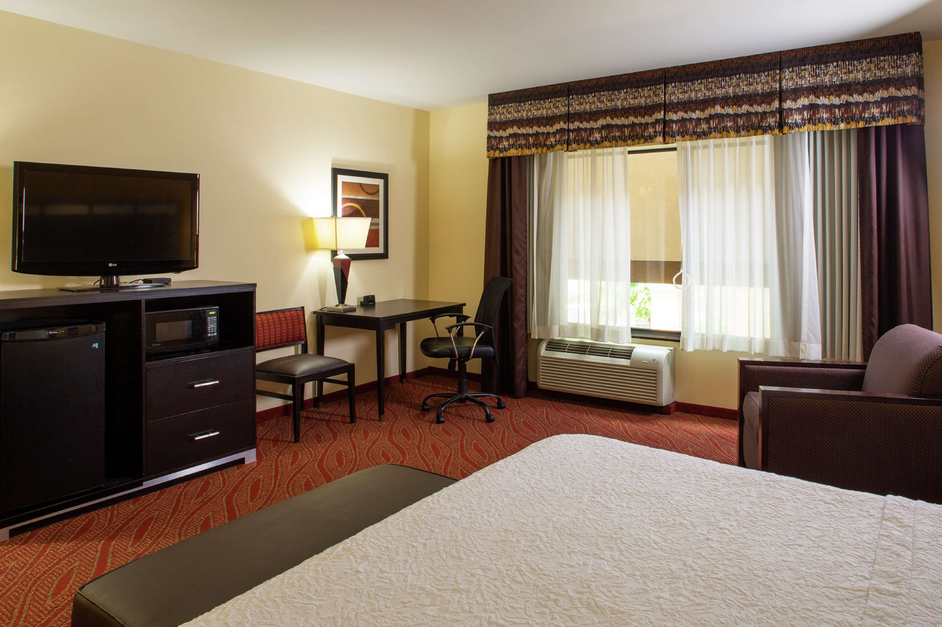A hotel room with a bed, desk, chair, television, and a minibar.
