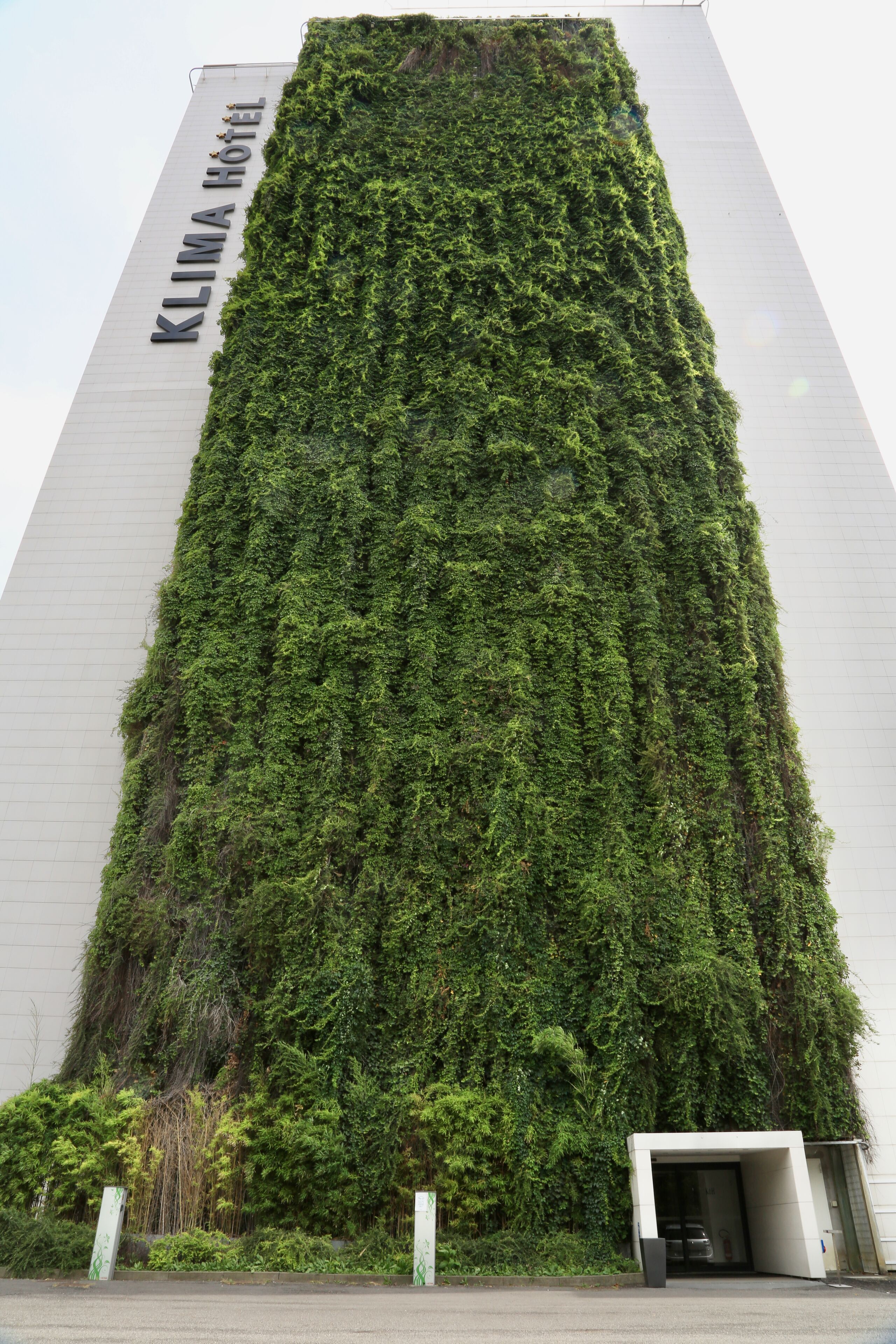 Un edificio de hotel alto con fachada de jardín vertical y el nombre "KLIMA HOTEL" en el lateral.