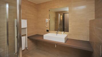 Une salle de bain moderne avec une douche à l’italienne en verre, un lavabo blanc et un grand miroir.