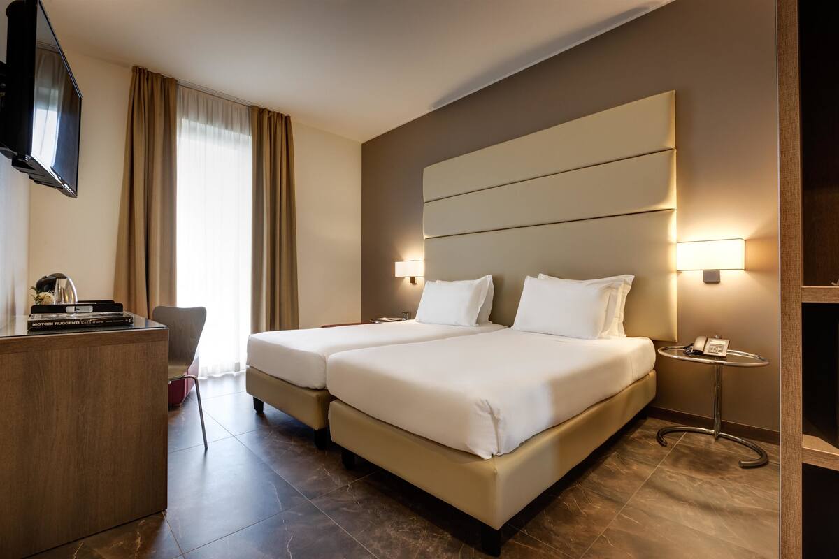 A hotel room with two beds, a desk, a TV, and a bedside table with a phone.