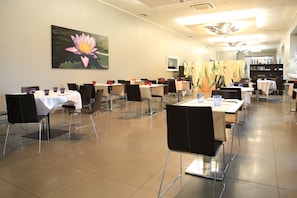 A conference room with tables and chairs, a large flower painting, and a bookshelf with books and bottles. - Klima Hotel Milano Fiere (Milan)