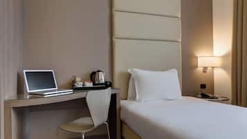 Habitación de hotel con cama, escritorio con computadora portátil, silla, mesita de noche con lámpara y otro buró.
