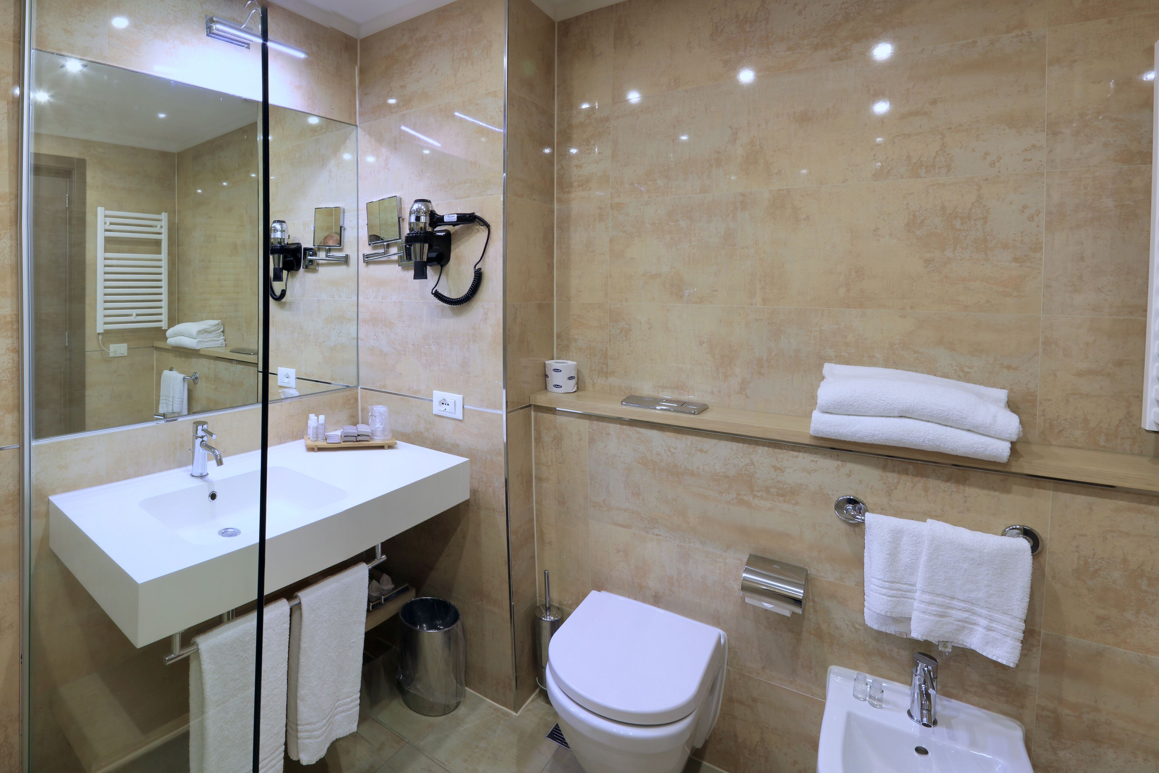 Un baño moderno con ducha de vidrio, lavamanos blanco, inodoro y espejo.