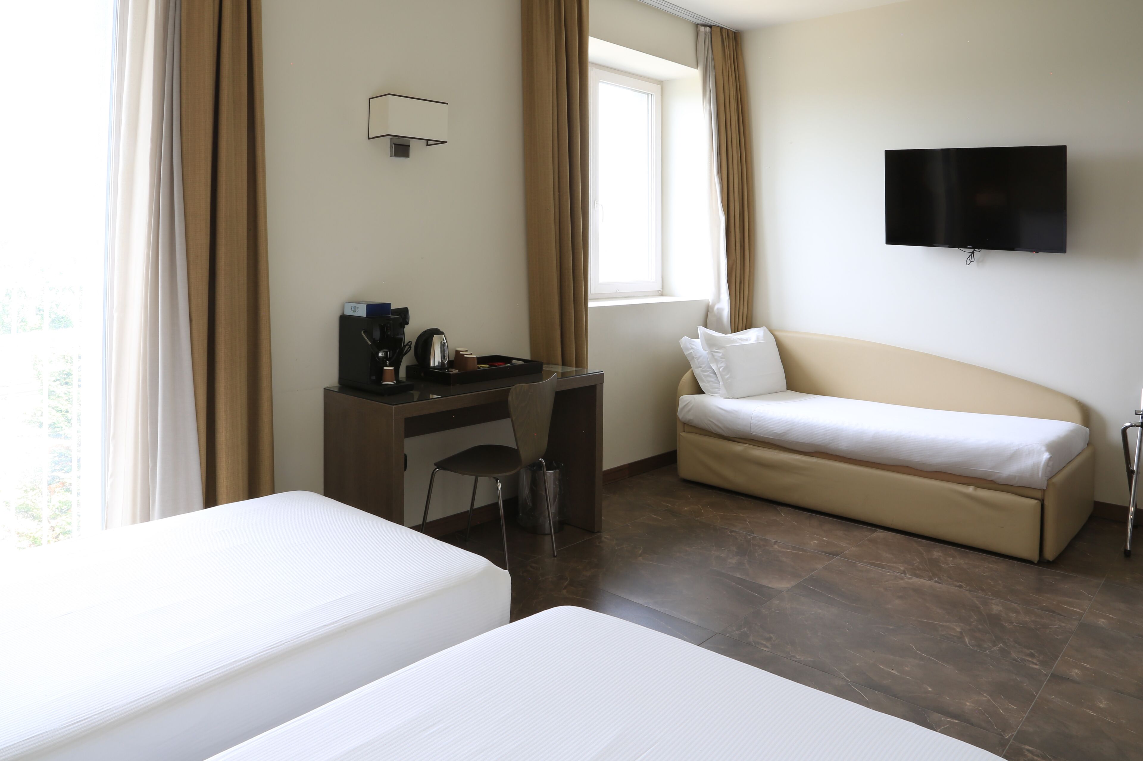 Een hotelkamer met een bed, een bureau met stoel, een televisie en een raam met gordijnen.