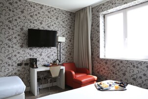 Et hotelværelse med et skrivebord, en rød stol, et fjernsyn og et spisebord med morgenmadsprodukter.