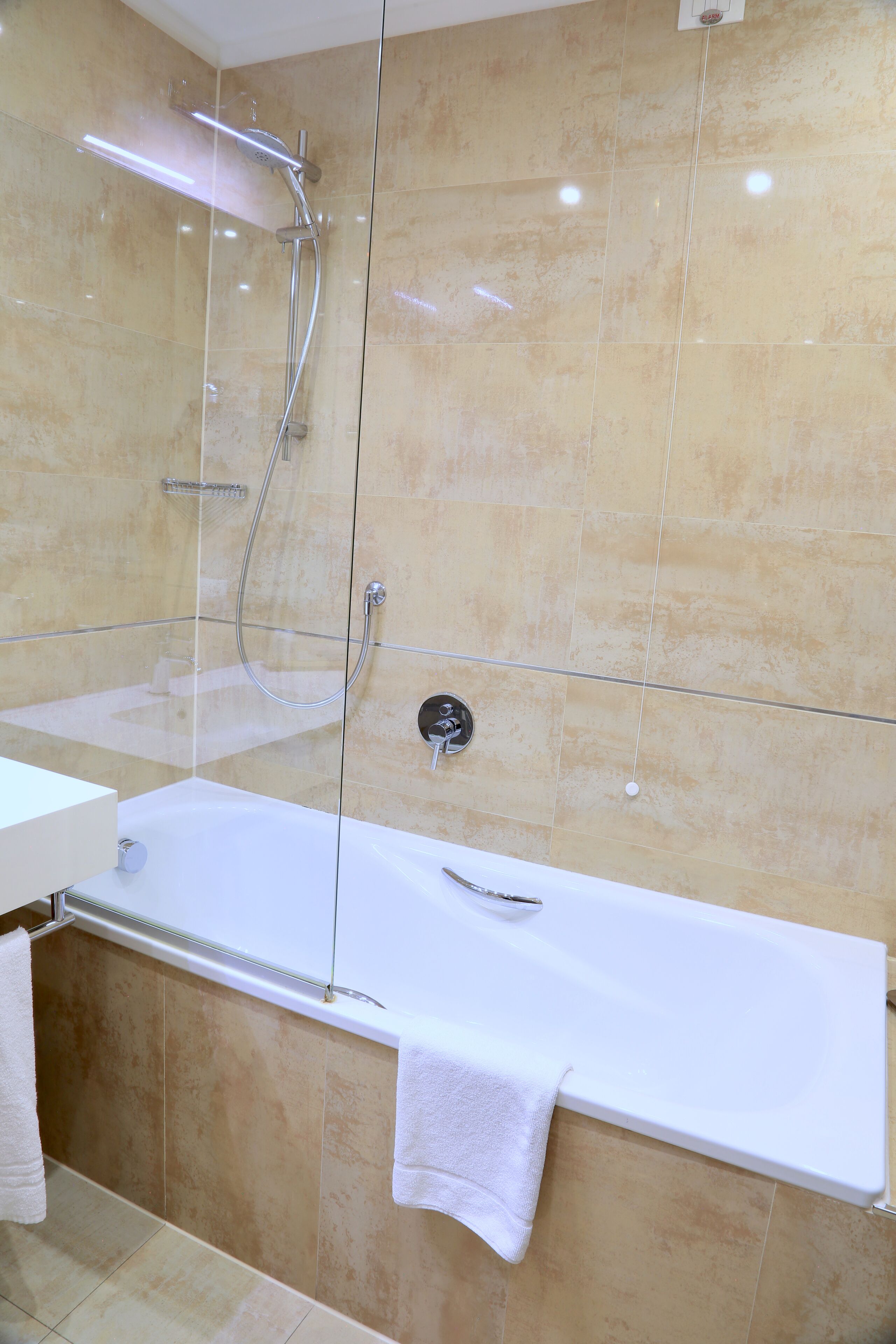 A modern bathroom with a glass-enclosed shower, a white bathtub, and beige tiles.