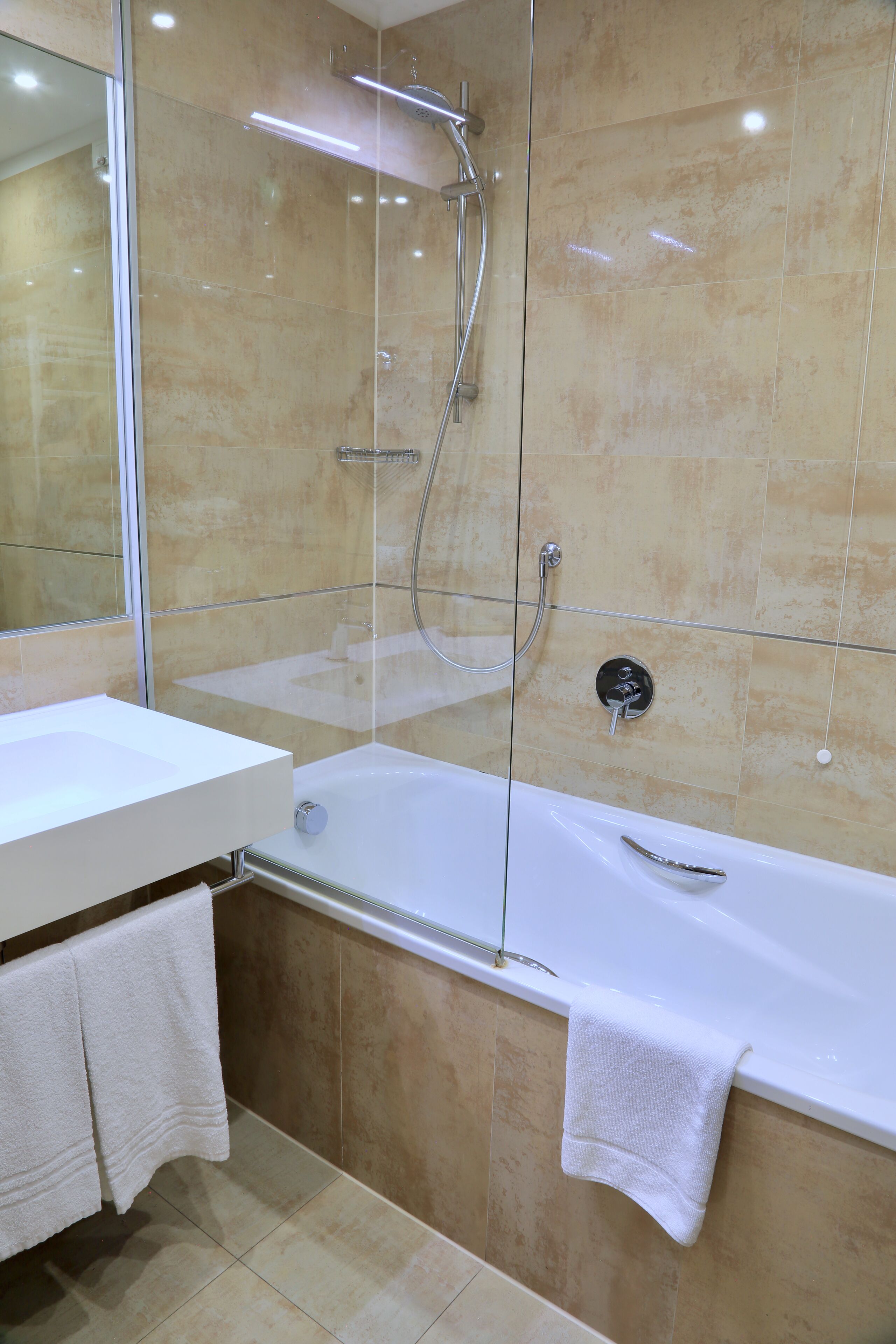 A modern bathroom with a glass-enclosed shower, a white bathtub, and a vanity with a mirror.