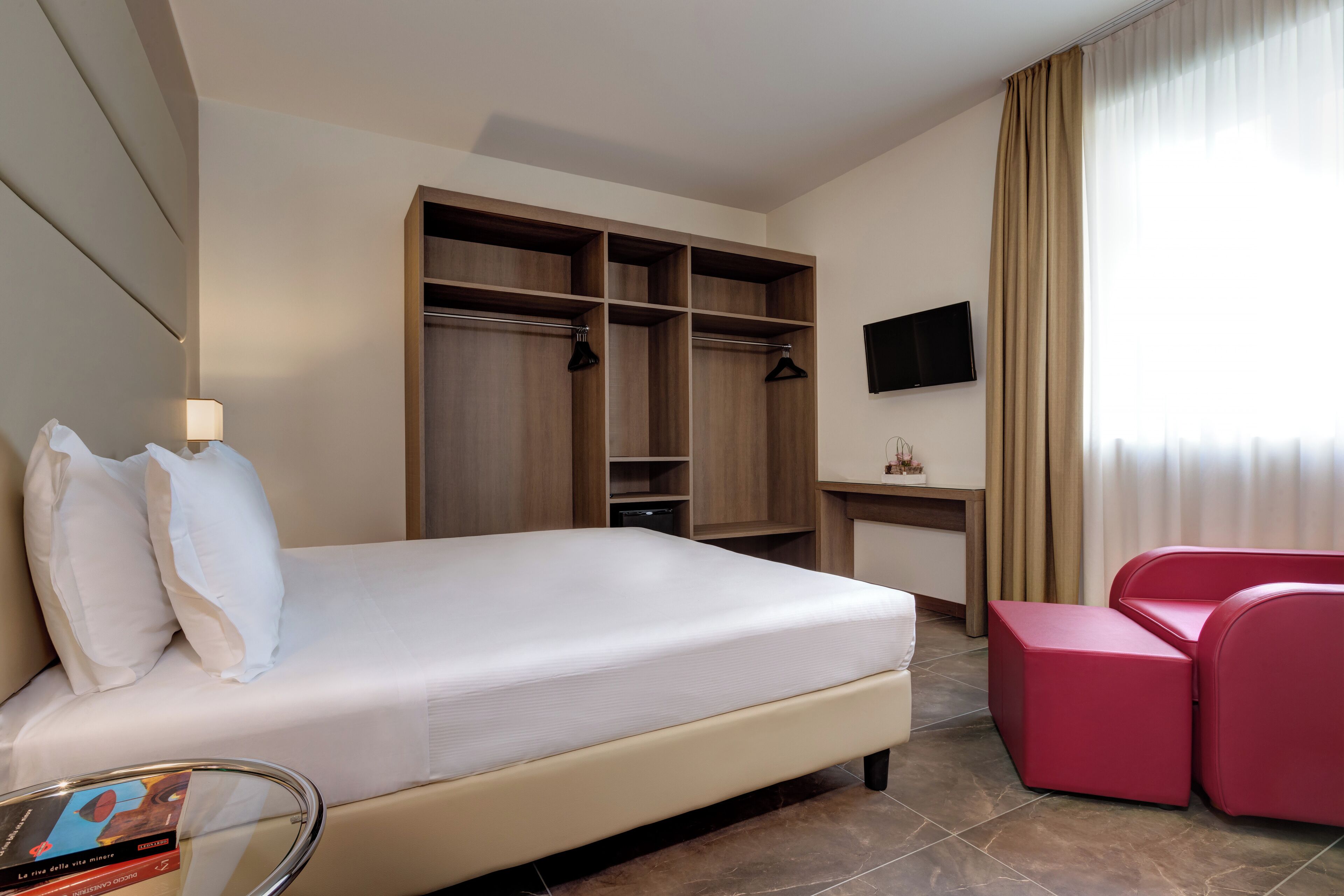 Een hotelkamer met een bed, een bureau, een televisie, een kledingkast en een rode stoel.