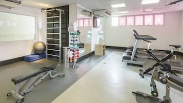 Un gimnasio con cintas de correr, una bicicleta estática, una máquina de remo, una barra de dominadas sujeta a la pared y una pelota medicinal fijada a la pared.