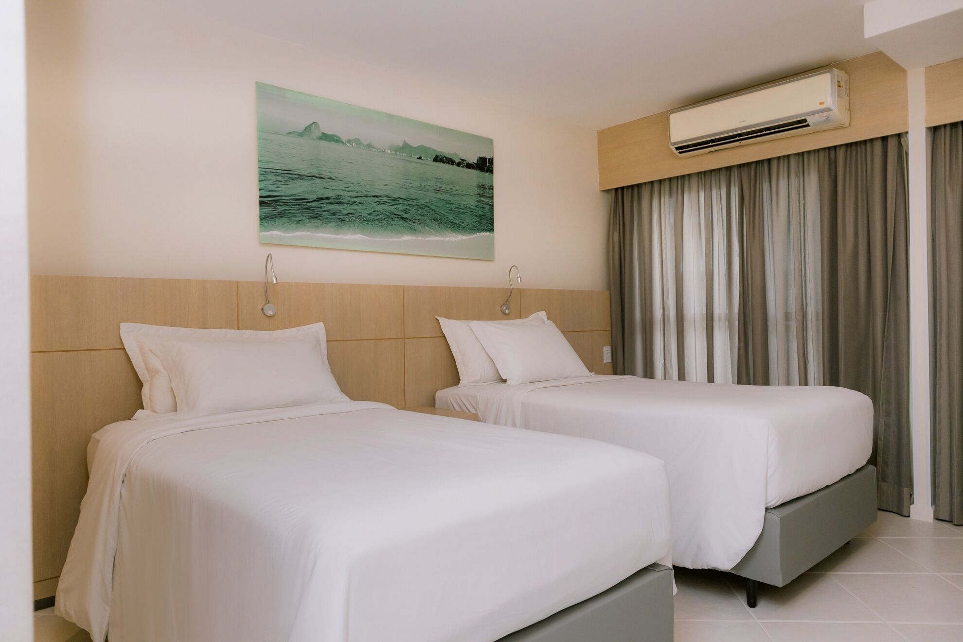 Habitación de hotel con dos camas, aire acondicionado instalado en la pared y un ventanal con cortinas.