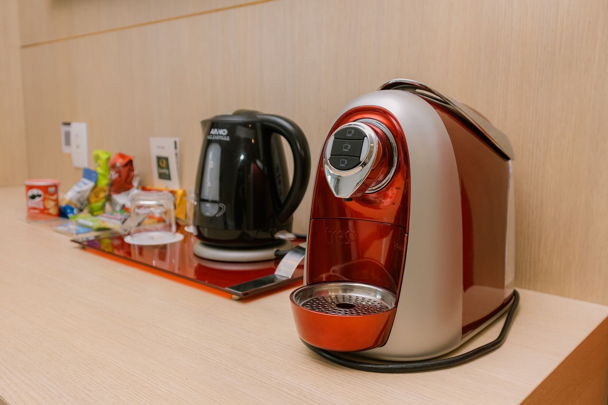 Una cafetera con portavasos y un hervidor sobre una mesa de madera.
