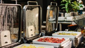 Un bufé con diferentes alimentos en recipientes de metal, una olla roja y una planta al fondo.